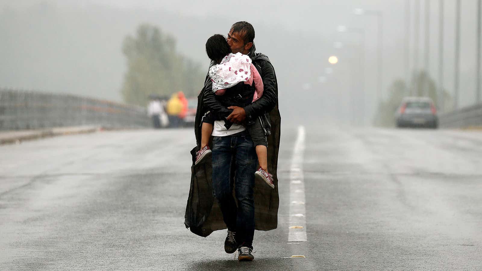 A Syrian father clutches his daughter as they cross the border from Greece into Macedonia in the rain.