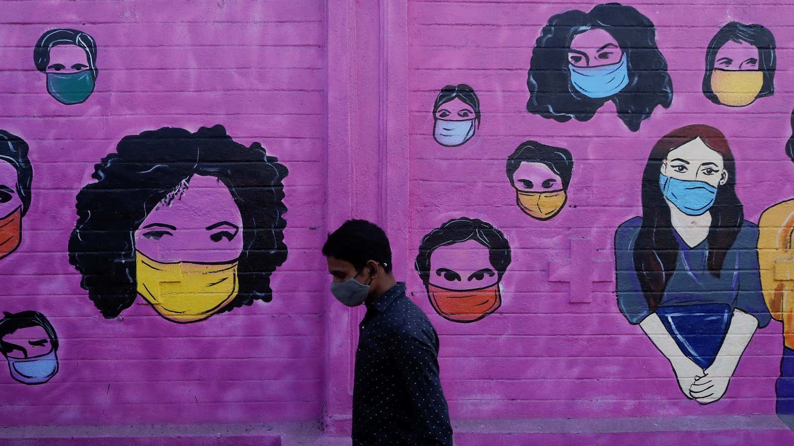 A man wearing a protective face mask walks past a mural on a street in Mumbai