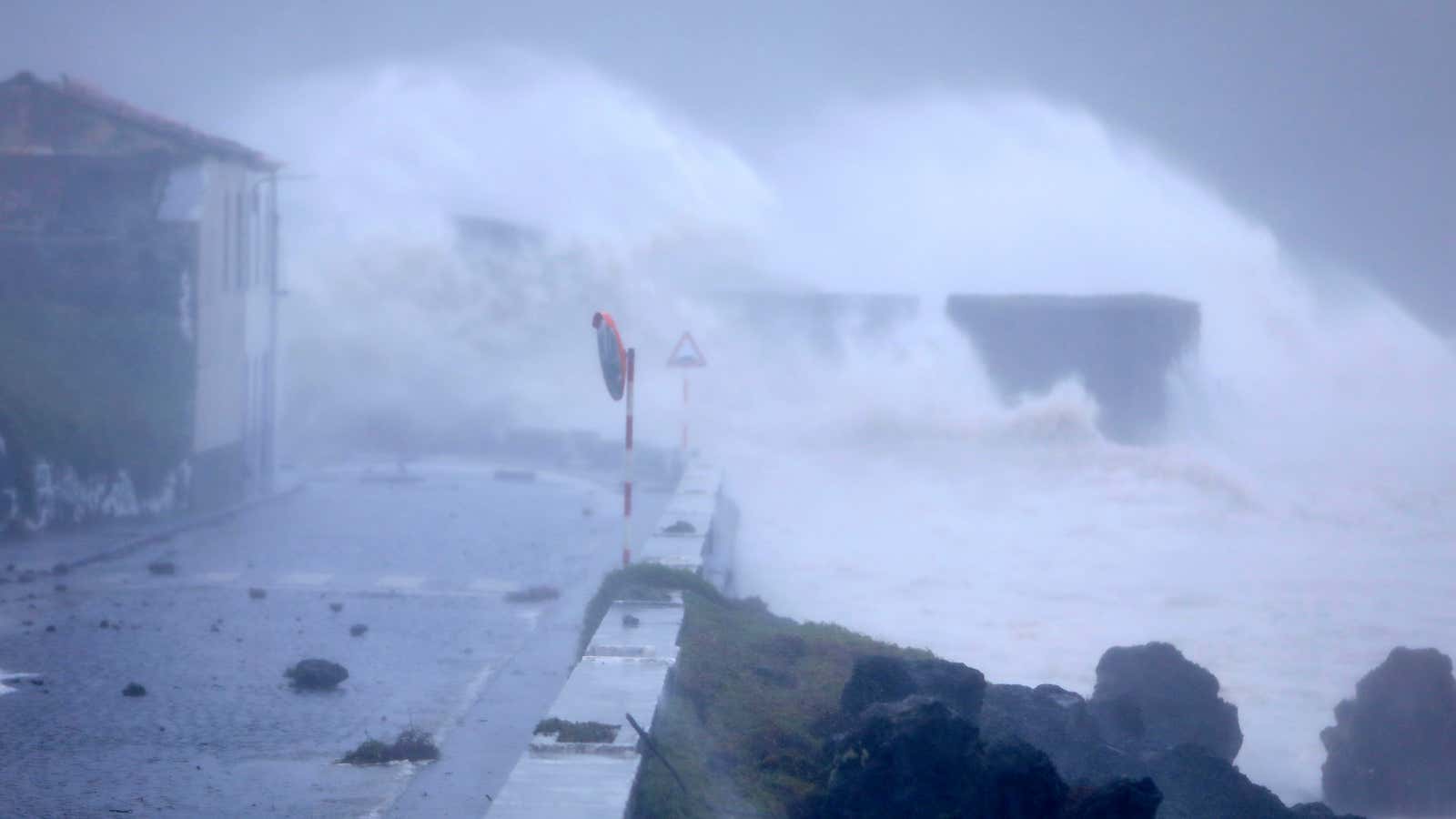 Waves crash on a seafront road in Horta.