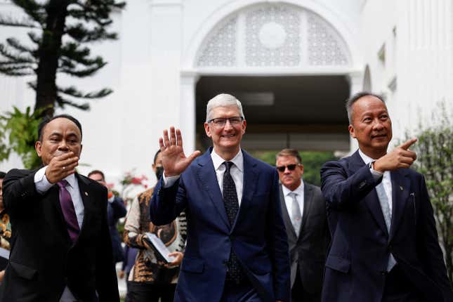 Tim Cook, au centre, souriant et saluant, les hommes des deux côtés de lui font également signe