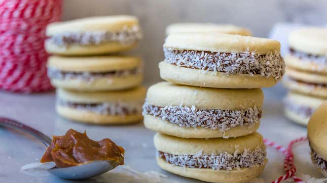 Alfajores cookies stacked on a table next to a spoonful of dulce de leche.