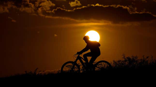 A cyclist tops a hill on a hot day at sunset, August 20, 2023, in San Antonio.