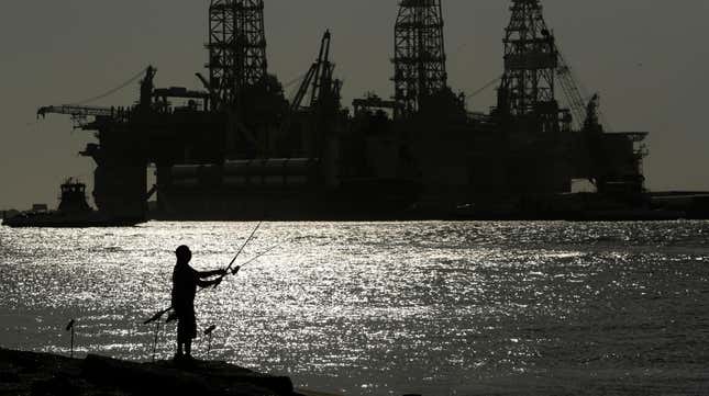 A person fishes in Port Aransas, Texas in front of an offshore oil drilling platform.