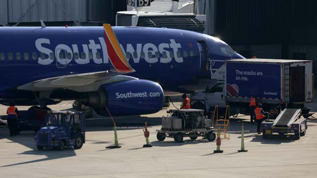 Southwest workers stand near baggage cars next to a Southwest jet.