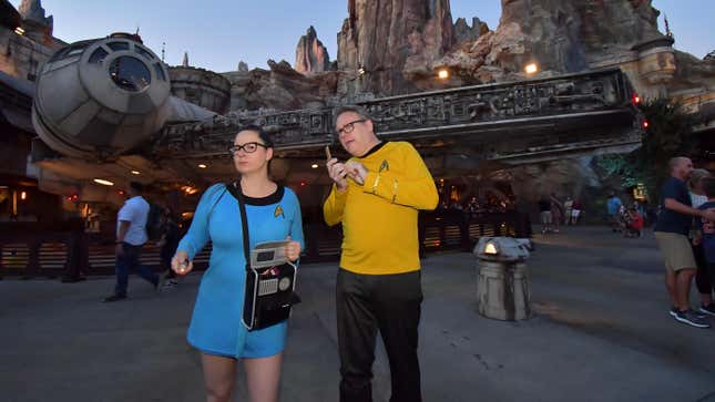 Two io9 readers dresses as classic Star Trek science and command officers pose in front of the Millennium Falcon at Disney's Star Wars: Galaxy's Edge, looking suitably confused by their whereabouts.