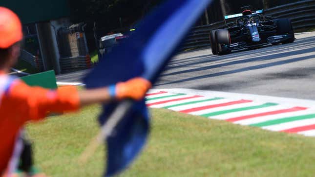 A photo of a marshal waving a blue flag as Lewis Hamilton drives past in his black Mercedes racer. 