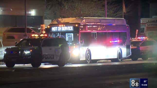 A Las Vegas bust sits stopped with a Not In Service sign on the front. Two police cars stand in front of and behind the bus with their lights on.