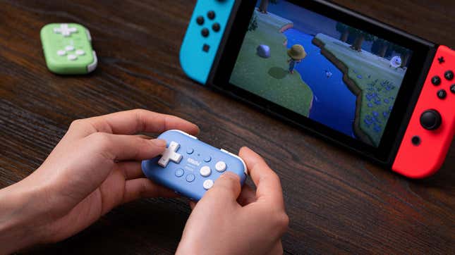 A person holding a blue 8BitDo Micro controller playing a game of Animal Crossing on a Nintendo Switch