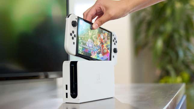 A photo shows someone taking a Switch OLED out of its dock.