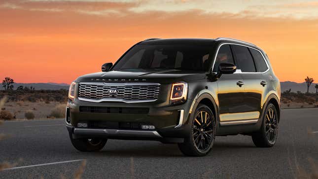 A view of the front quarter of a Kia Telluride parked on a desert road in the sunset, with the daytime running lights on.
