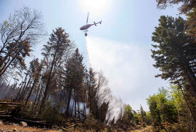 A helicopter contracted by the province drops water on a hot spot in Yankeetown, Nova Scotia, as an excavator makes a fire break, Thursday, June 1, 2023.