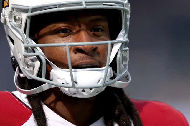 A Black man with long braids wears a white football helmet and red and white uniform as he gazes past the camera.