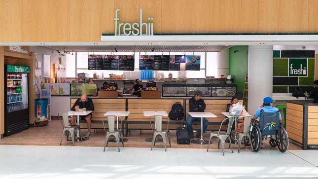 People sit down to eat at a Freshii in Toronto, Canada. Employees work in the background behind the counter.