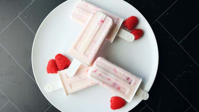 Popsicles on a plate with scattered raspberries.