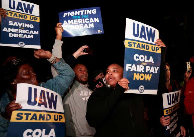Striking auto workers hold up signs that read "Fighting for the American dream" and "UAW stand up COLA and fair pay now"