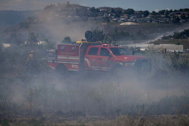 Firefighters battle a grass fire burning on an acreage behind a residential property in Kamloops, British Columbia, on June 5, 2023.