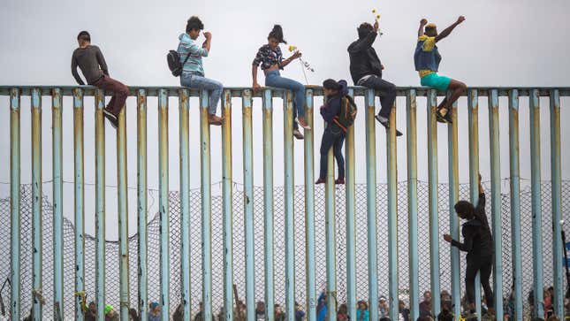 People climb a section of border fence to look toward supporters in the U.S. as members of a caravan of Central American asylum seekers arrive to a rally on April 29, 2018 in Tijuana, Baja California Norte, Mexico
