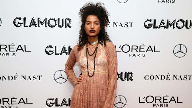 Actor Indya Moore wears a pink-peach colored dress with a dark necklace at a red carpet event.