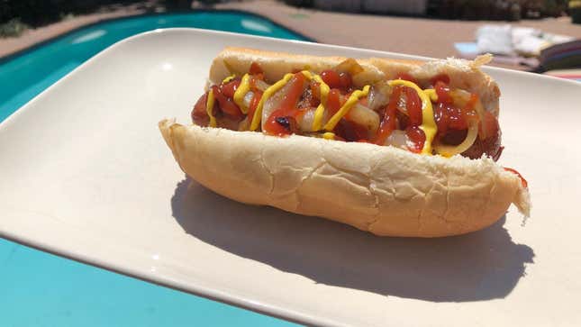 A hot dog with ketchup, mustard, and onions on a plate.
