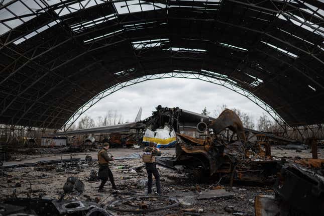 journalists photograph the remains of the Antonov An-225 airplane in a wrecked hanger at Hostomel airfield