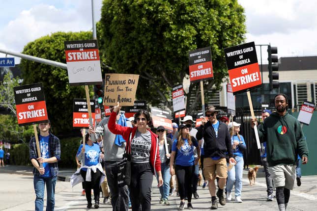 A group of protestors walks towards the camera holding signs that read "Writers Guild of America on strike!"
