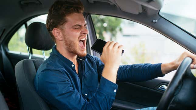 A bearded man sings into his phone with his eyes closed while driving a car