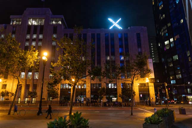 A bright white 'X' logo is seen on the top of the X Corp (formerly Twitter) office building at night.