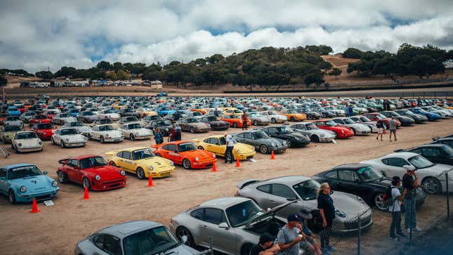 A vast dirt parking lot is filled with Porsche models of all colors and generations