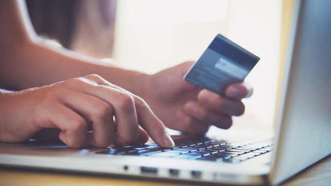 A person holds a credit card in one hand and types on a laptop with the other hand.