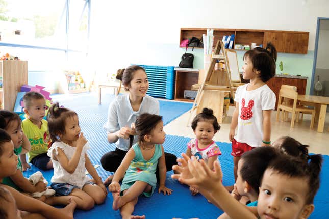 A OneSky caregiver sits on the ground, playing with a group of kids