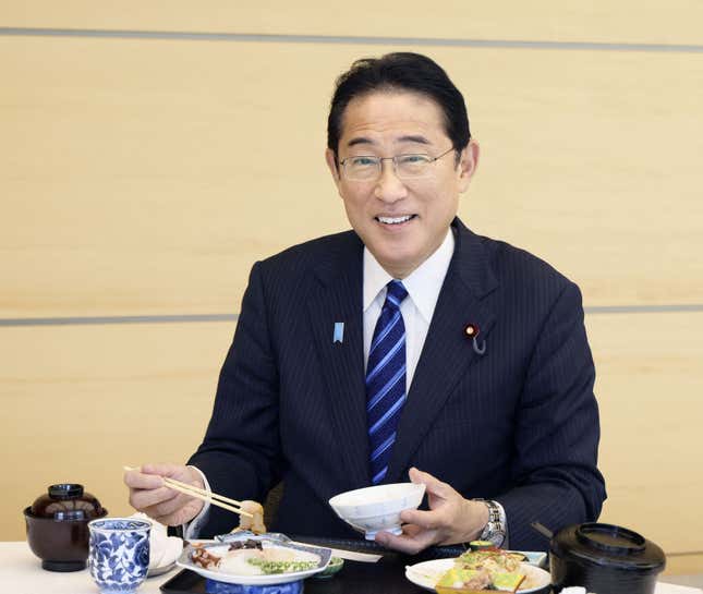Japanese prime minister Fumio Kishida eating sashimi and smiling.