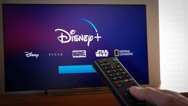 A television showing the Disney+ logo with Disney Pixar Marvel Star wars and National Geographic also labeled. A person points a remote toward the screen.