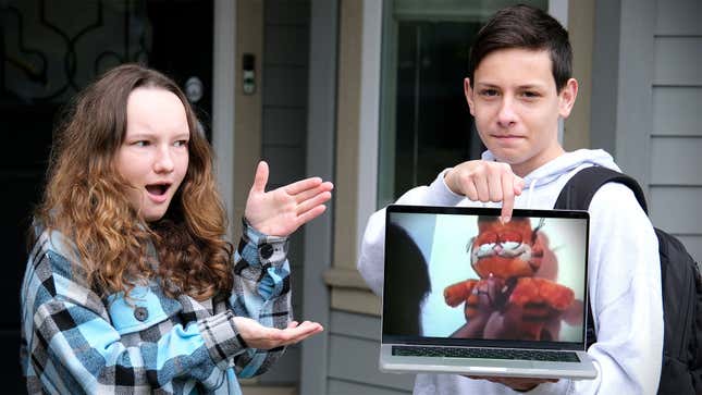 A photo shows two kids holding a laptop playing a video of Garfield being crucified. 