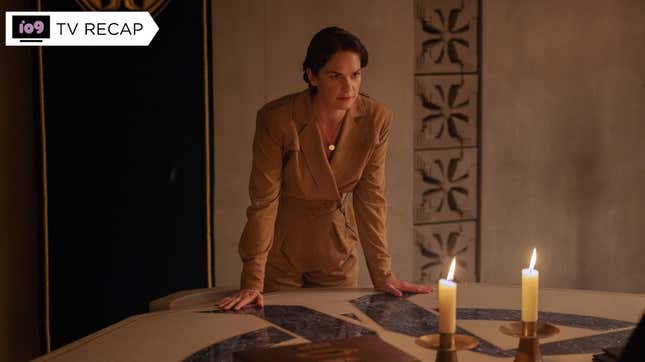 Mrs. Coulter (Ruth Wilson) leans onto a table holding a pair of candles