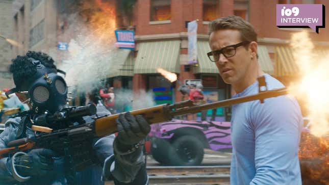 A player in Free Guy's Free City game wears a gasmask and shooting a rifle as Ryan Reynold's Guy walks by curious in a blue long sleeve shirt and black framed glasses.