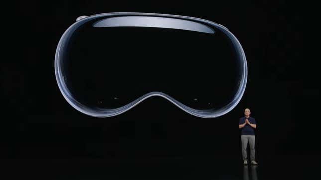 An image shows a man standing next to a large image of Apple's headset. 