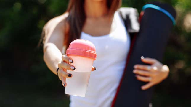 Woman holding shaker of clear whey.