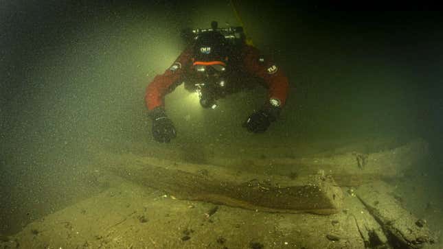 A diver in red approaches shipwreck timber underwater.