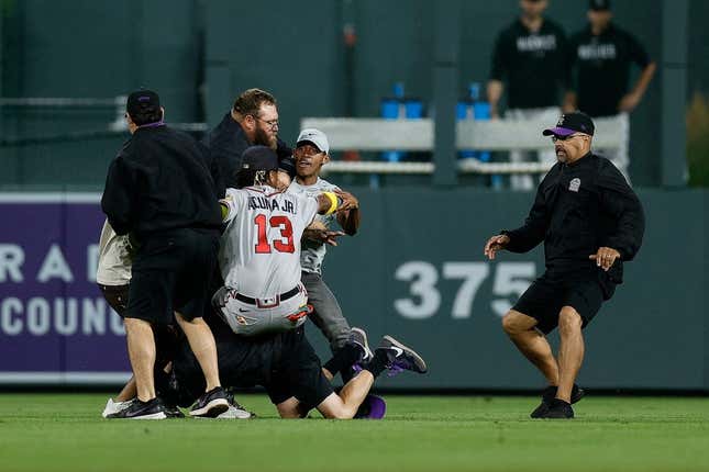 Aug 28, 2023; Denver, Colorado, USA; A fan charges at Atlanta Braves right fielder Ronald Acuna Jr. (13) as grounds crew detains another person in the seventh inning against the Colorado Rockies at Coors Field.