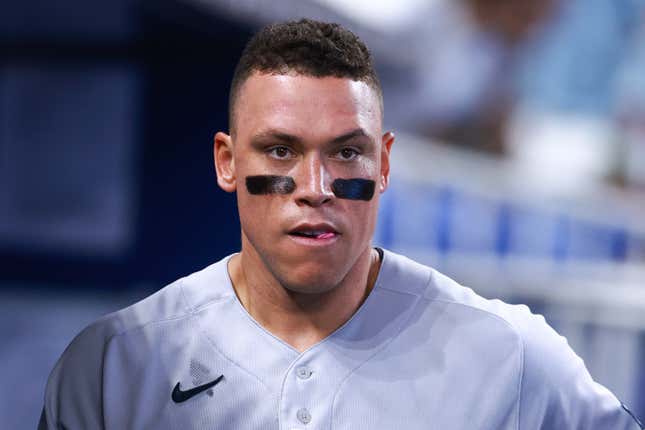 A man with brown curly hair and eye black under both eyes in a gray Yankees baseball uniform looks stunned.