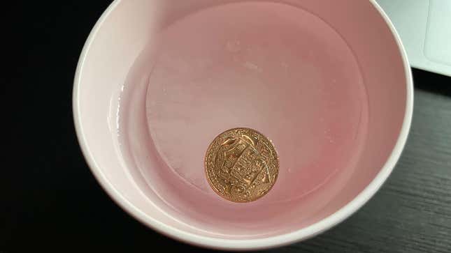 Pink cup with a penny on top of ice, but the ice is partially melted