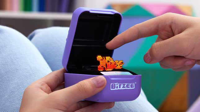 A user holding the Bitzee digital pet and touching the character with their finger.