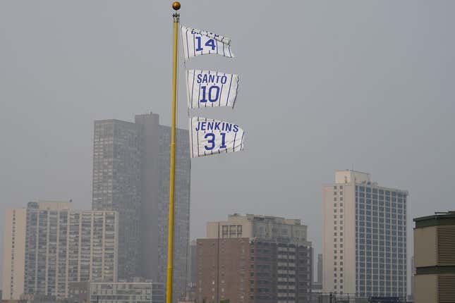 Jun 27, 2023; Chicago, Illinois, USA; The flags of Chicago Cubs&#39; Hall of Fame players Ernie Banks (14), Ron Santo (10) and Ferguson Jenkins fly off the Wrigley Field left field foul pole as a veil of haze from Canadian wildfires shroud high rise buildings along Lake Michigan before a baseball game between the Cubs and the Philadelphia Phillies at Wrigley Field.