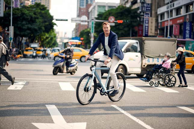 Ties Carlier, co-founder of Dutch electric bike maker Vanmoof, rides a bike across an intersection in what appears to be Taiwan.