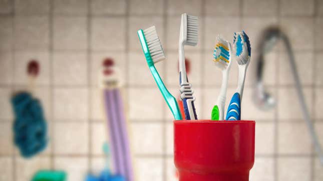 A cup filled with several  toothbrushes sitting on a bathroom sink