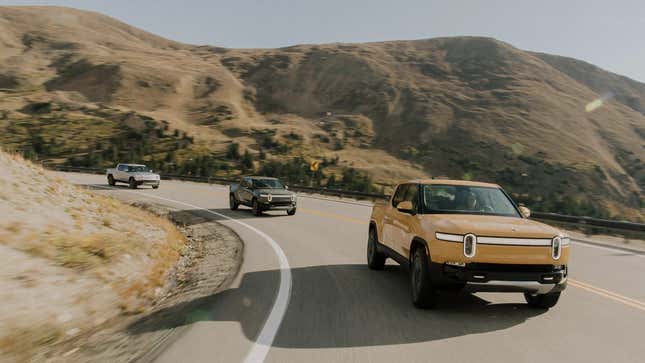 Three Rivian R1Ts driving down a road.