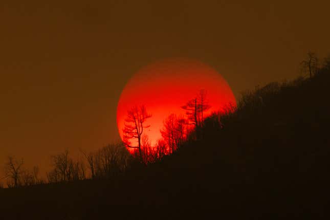 The sun sinks behind a smoky sky and burned forest near Mariposa, California.
