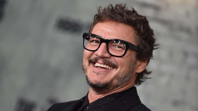 A smiling Pedro Pascal wearing a black button up shirt and glasses
