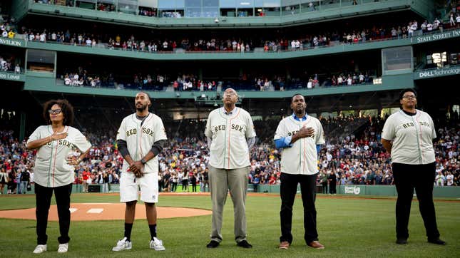 For Black men and a Black woman are shown on the field at Fenway Park, two with hands over their hearts, all wearing Juneteenth Red Sox jerseys.