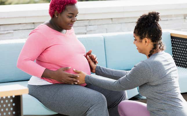 Pregnant woman with doula touching baby bump